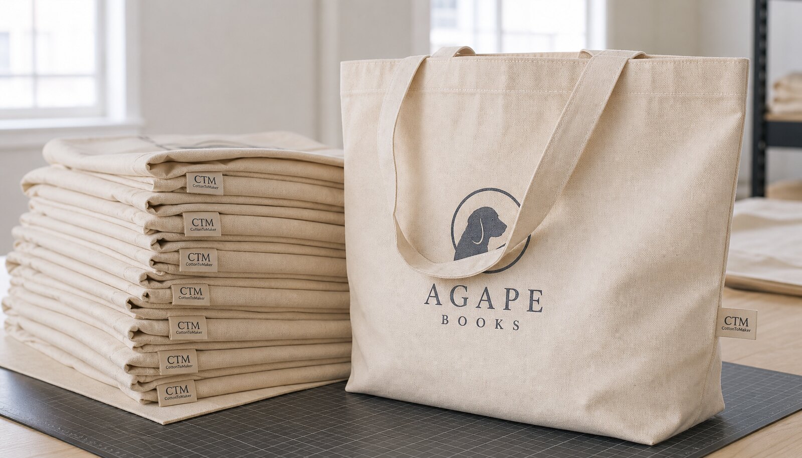 Stack of natural canvas book fair totes with a simple CTM woven side label in a factory sample room