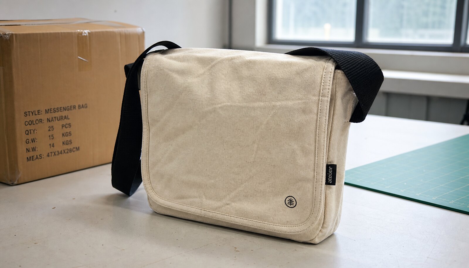 Photorealistic canvas commuter messenger bag with a simple CTM/CottonToMaker side label in a clean factory sample room.