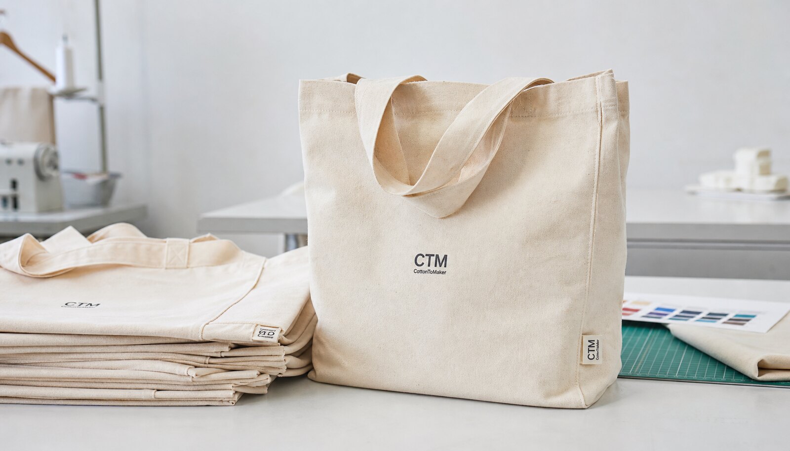 Natural canvas grocery totes with a simple CTM sample logo in a clean factory sample room