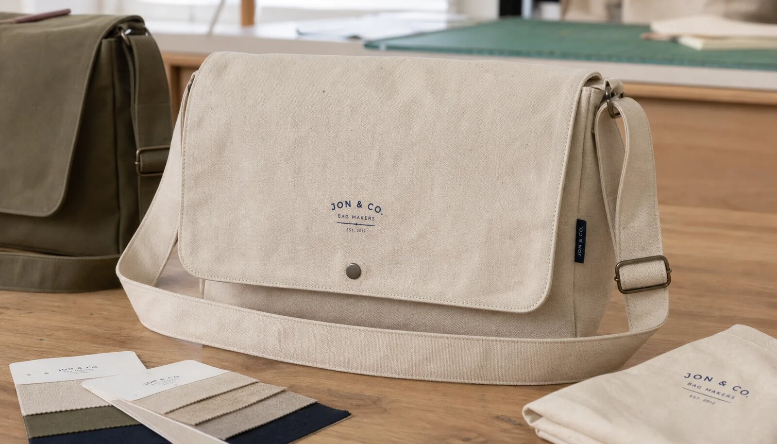 Natural canvas messenger bag sample with CTM logo and CottonToMaker woven side label on a studio sample table