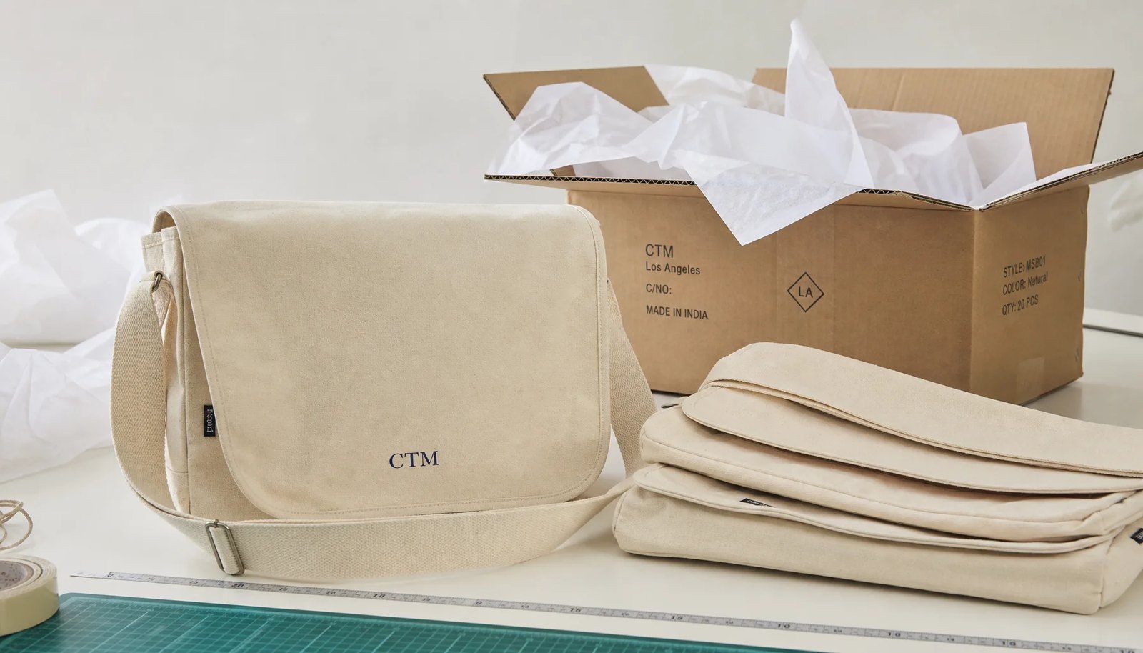 Custom canvas messenger bag with CTM logo packed beside export carton for university bookstore orders