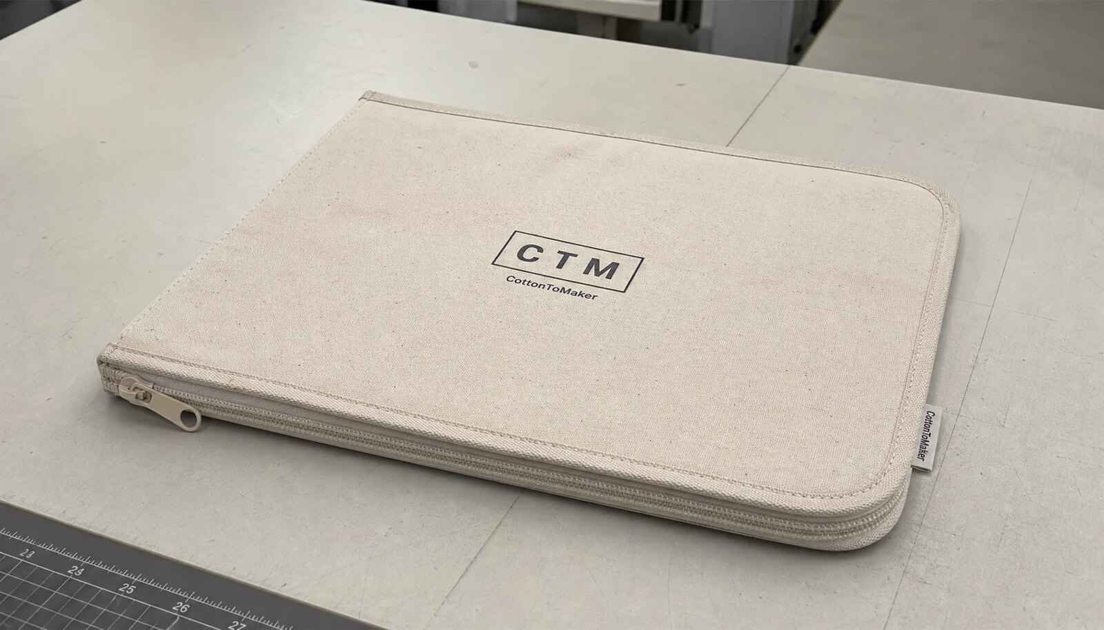 Natural cotton canvas zipper portfolio with printed CTM logo, coil zipper, and neat stitching on a factory sample table