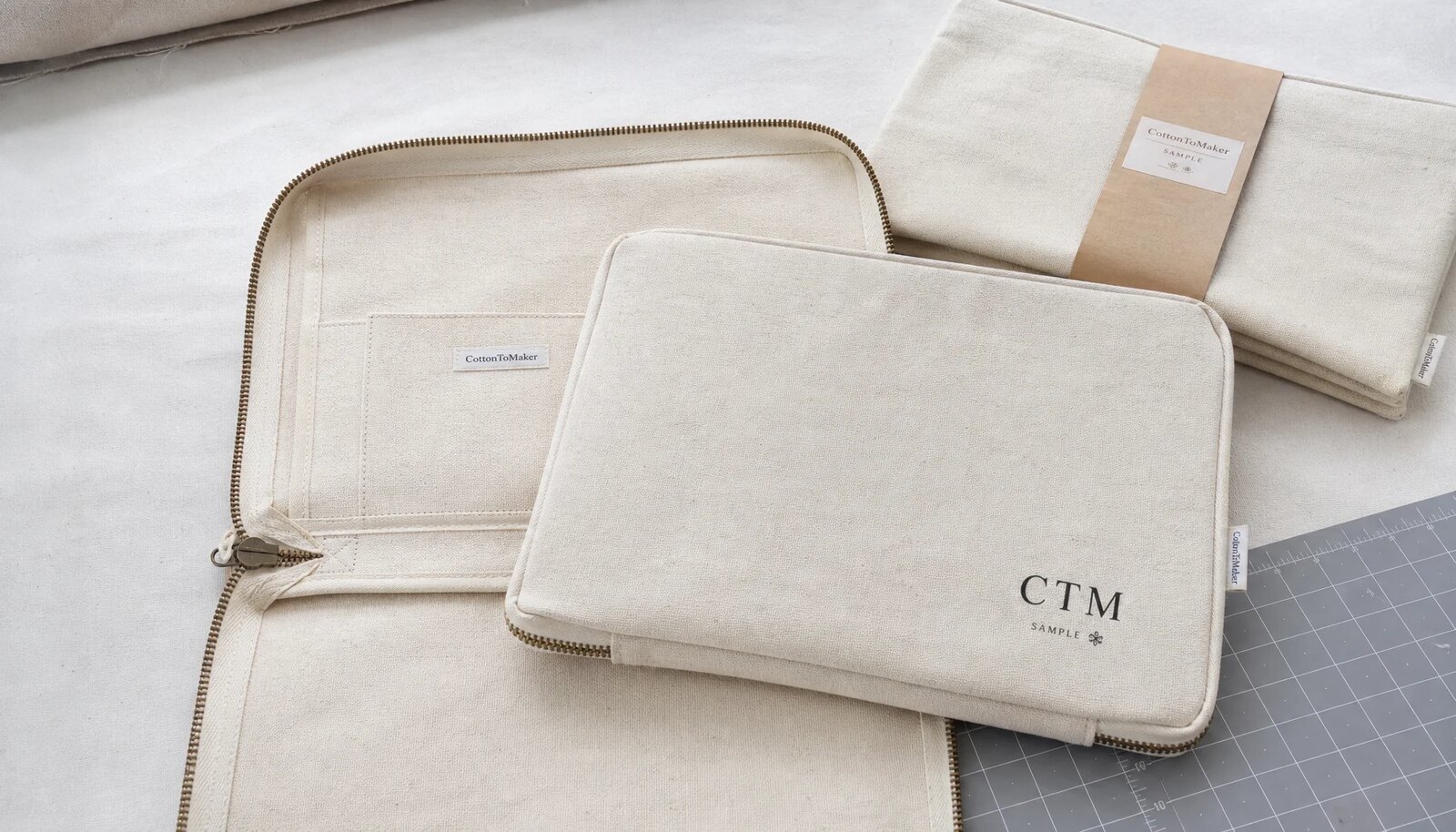 Natural canvas zipper portfolios with printed logo, woven side label, zipper, lining, and reinforced stitching details