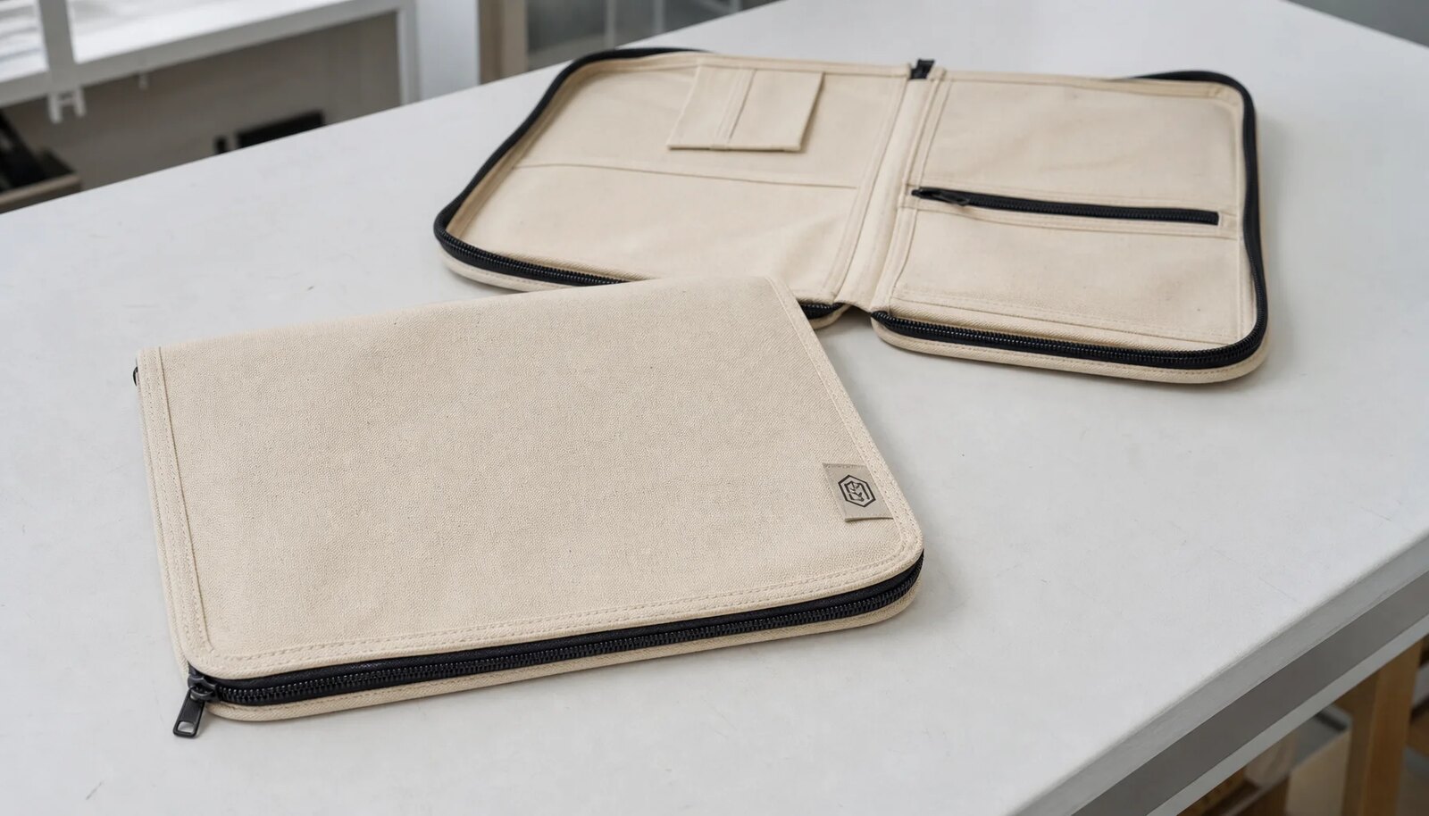 Photorealistic canvas zipper portfolio with a stitched CTM side label in a factory sample room.