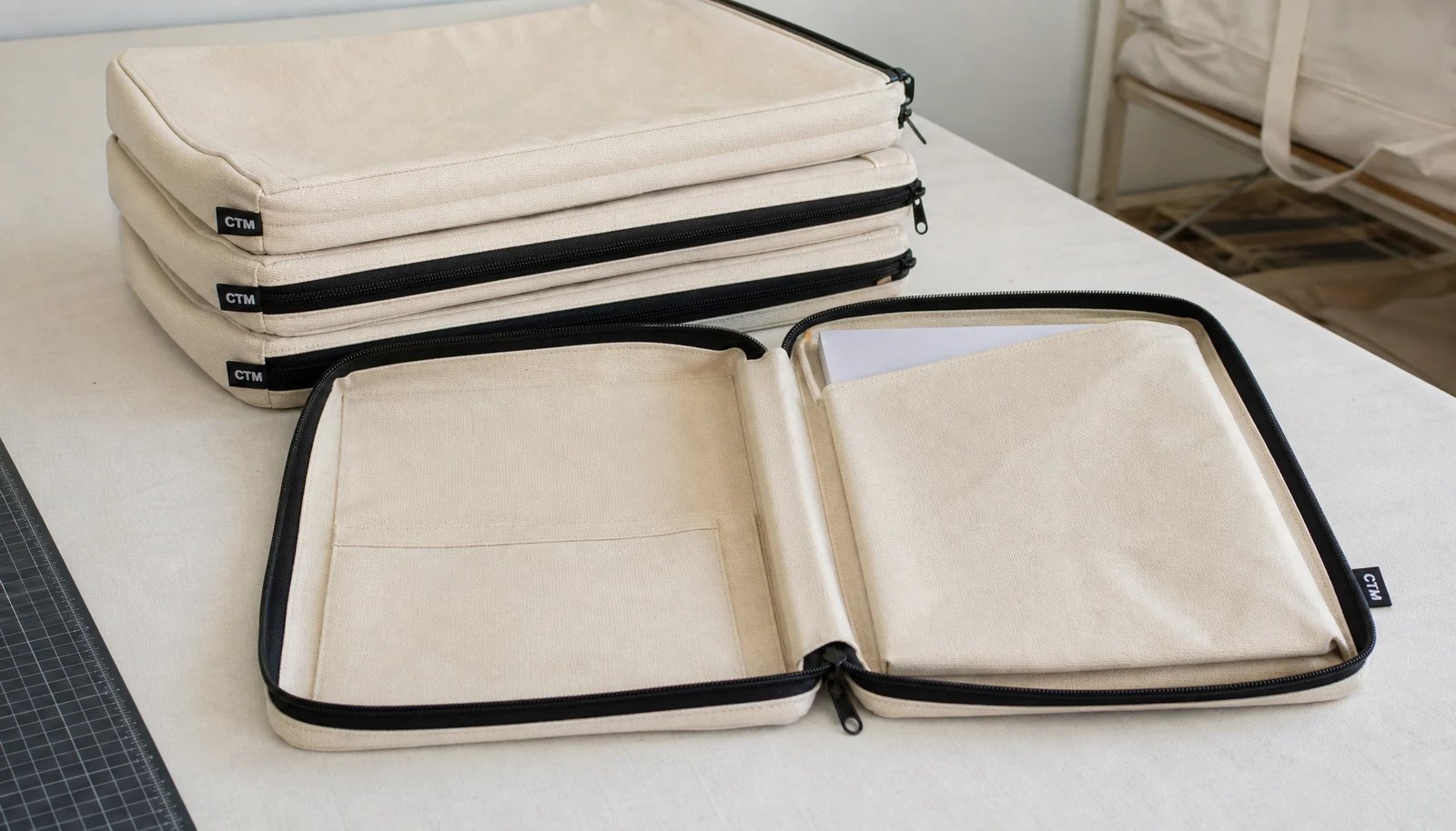 Natural canvas zipper portfolios with CTM woven side label and black zipper in a clean studio setting