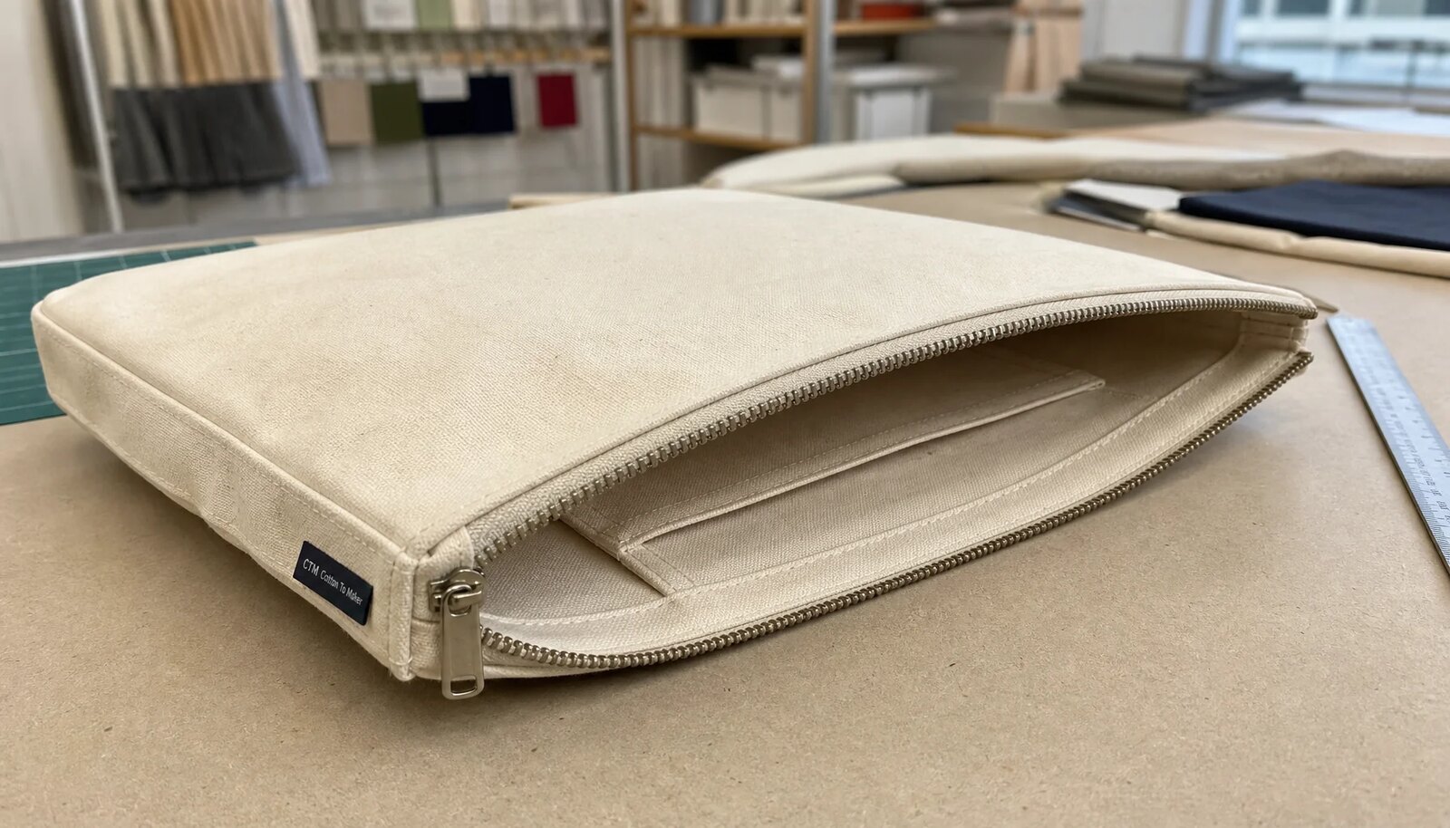 Natural canvas zipper portfolio sample with CTM woven side label in a factory sample room