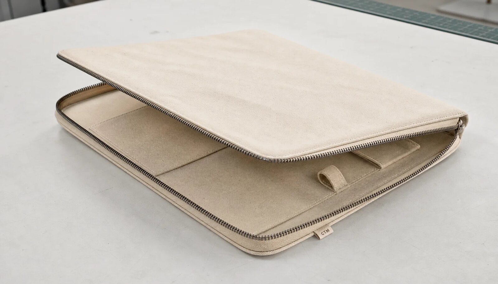 Photorealistic canvas zipper portfolio with a stitched CTM sample label in a clean sample room