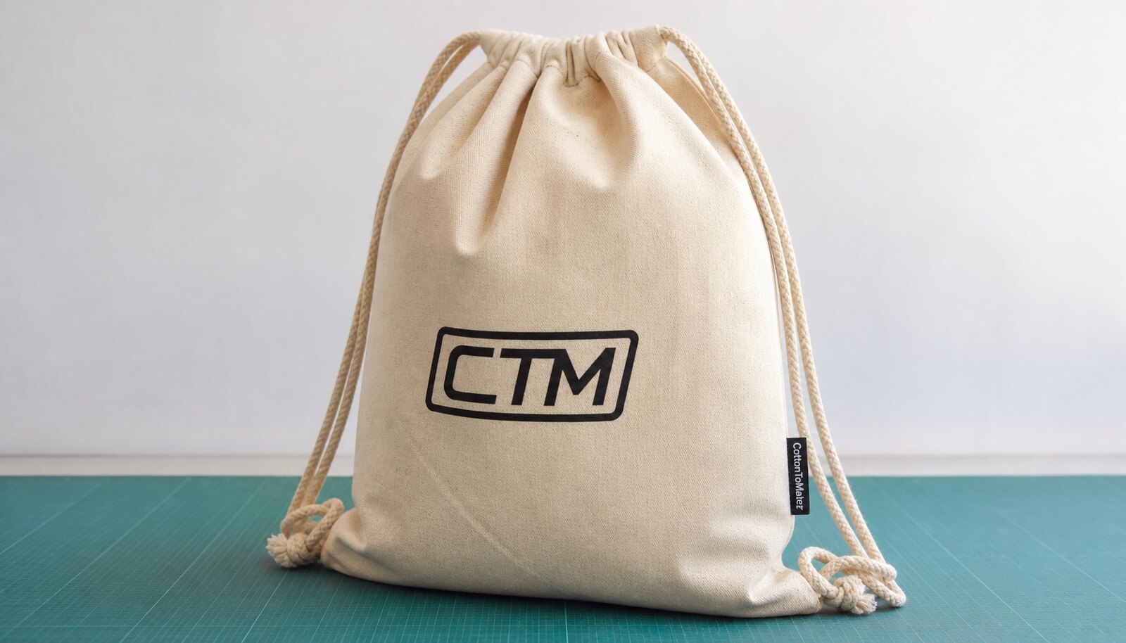 Photorealistic cotton drawstring backpack sample with a CTM logo printed on the front and a woven side label in a clean factory room