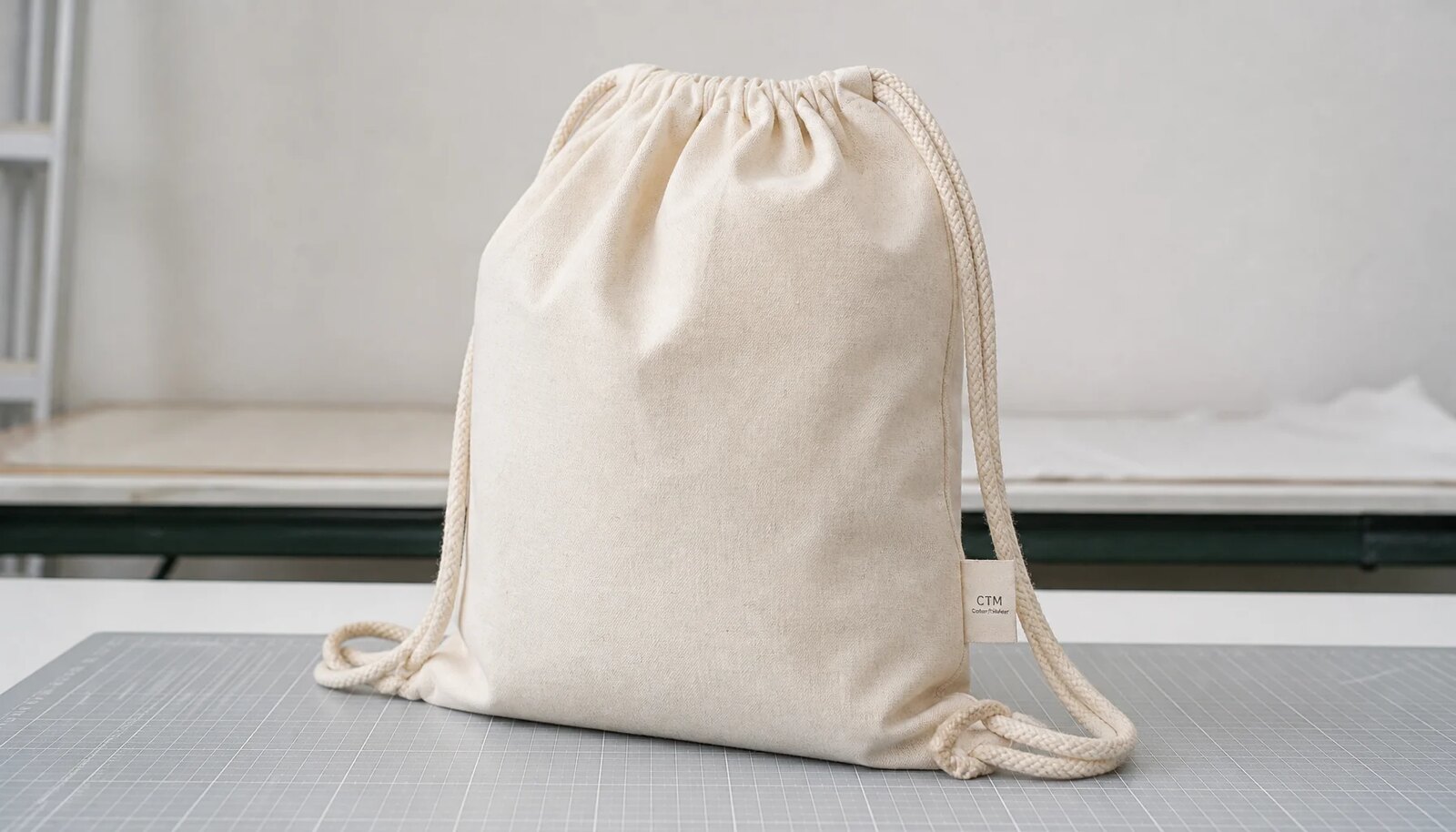 Natural cotton drawstring backpack with reinforced cord exits and a small CTM woven side label in a clean factory sample room