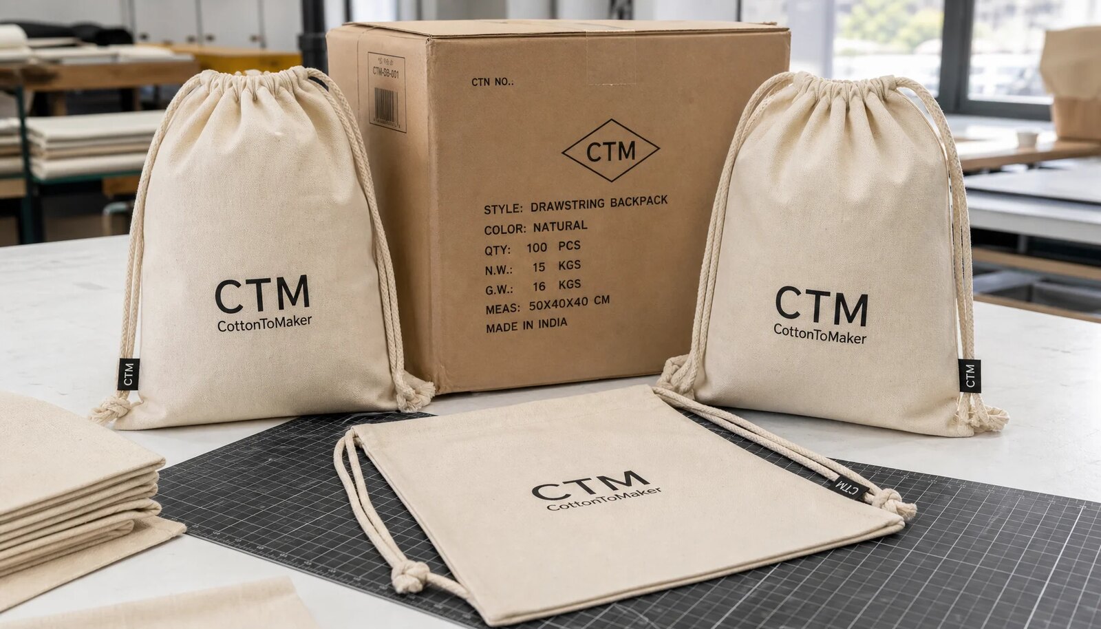 Cotton drawstring backpacks beside a kraft export carton in a factory sample room.