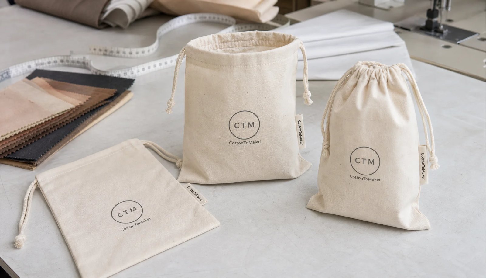 Natural cotton drawstring pouches with CTM sample logo and CottonToMaker side label in a factory sample room