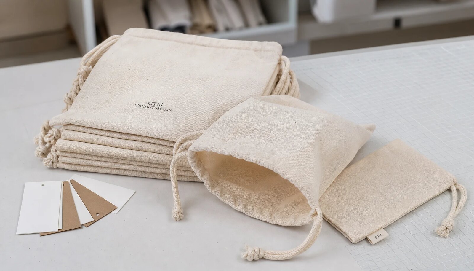 Natural cotton drawstring pouches with a small CTM sample logo in a clean sample room.