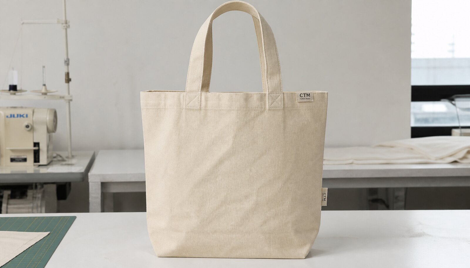 Natural canvas tote bag with a small CTM/CottonToMaker side label in a factory sample room
