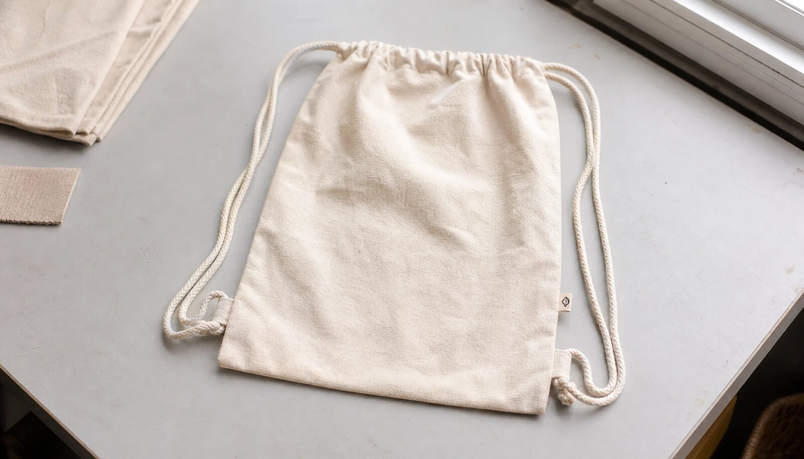 Natural cotton drawstring backpack with a simple CTM CottonToMaker logo, photographed in a clean factory sample room.