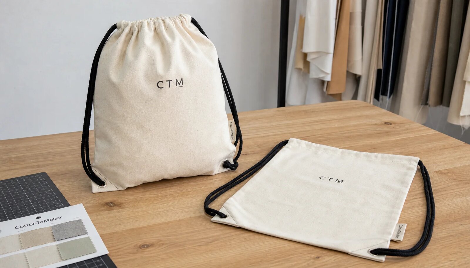 Natural cotton drawstring backpacks with CTM logo print and CottonToMaker side label on a sample table