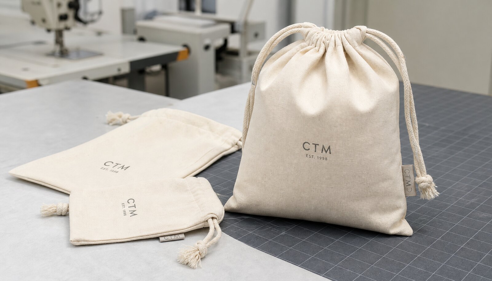 Natural cotton gift drawstring pouches with a small CTM sample logo in a clean factory sample room.