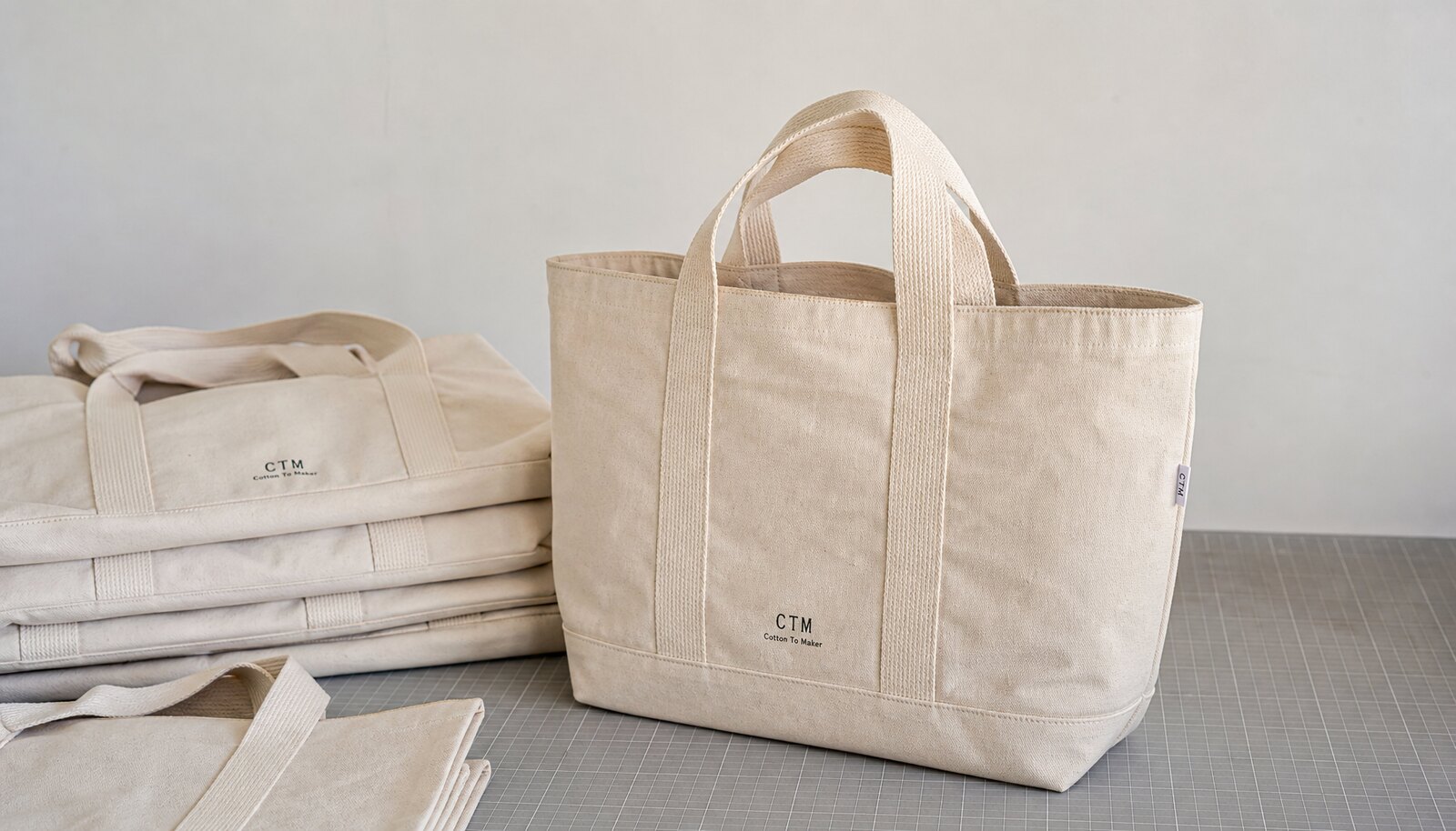 Large natural canvas grocery bag with a small CTM sample logo printed on the front in a clean factory sample room