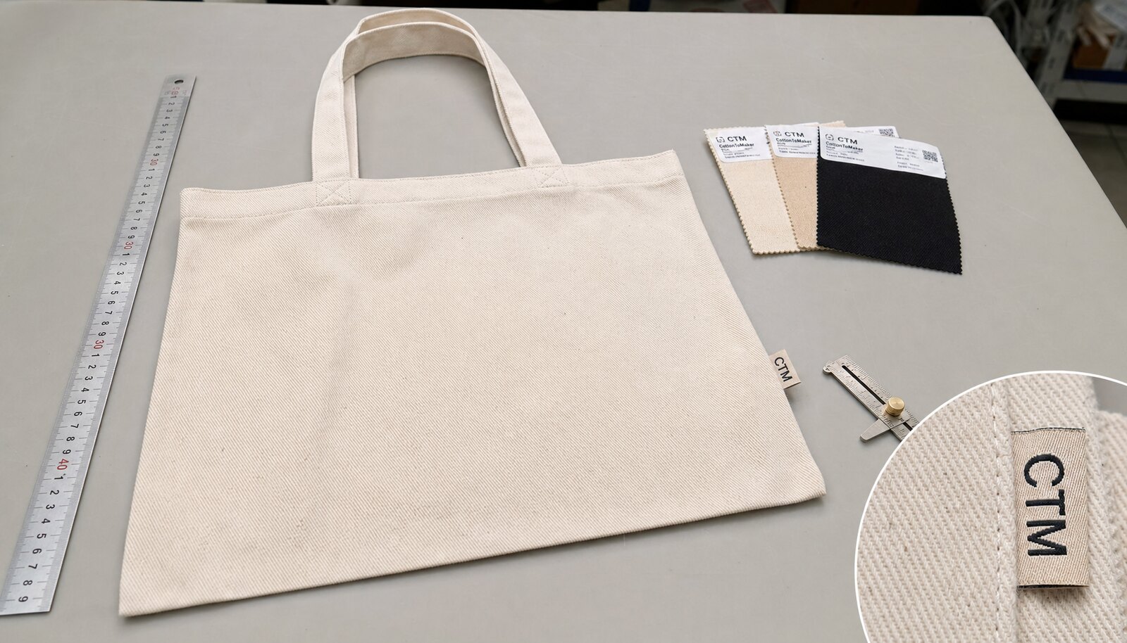 Natural organic cotton tote bag with stitched handles and a sewn CTM side label in a factory sample room.