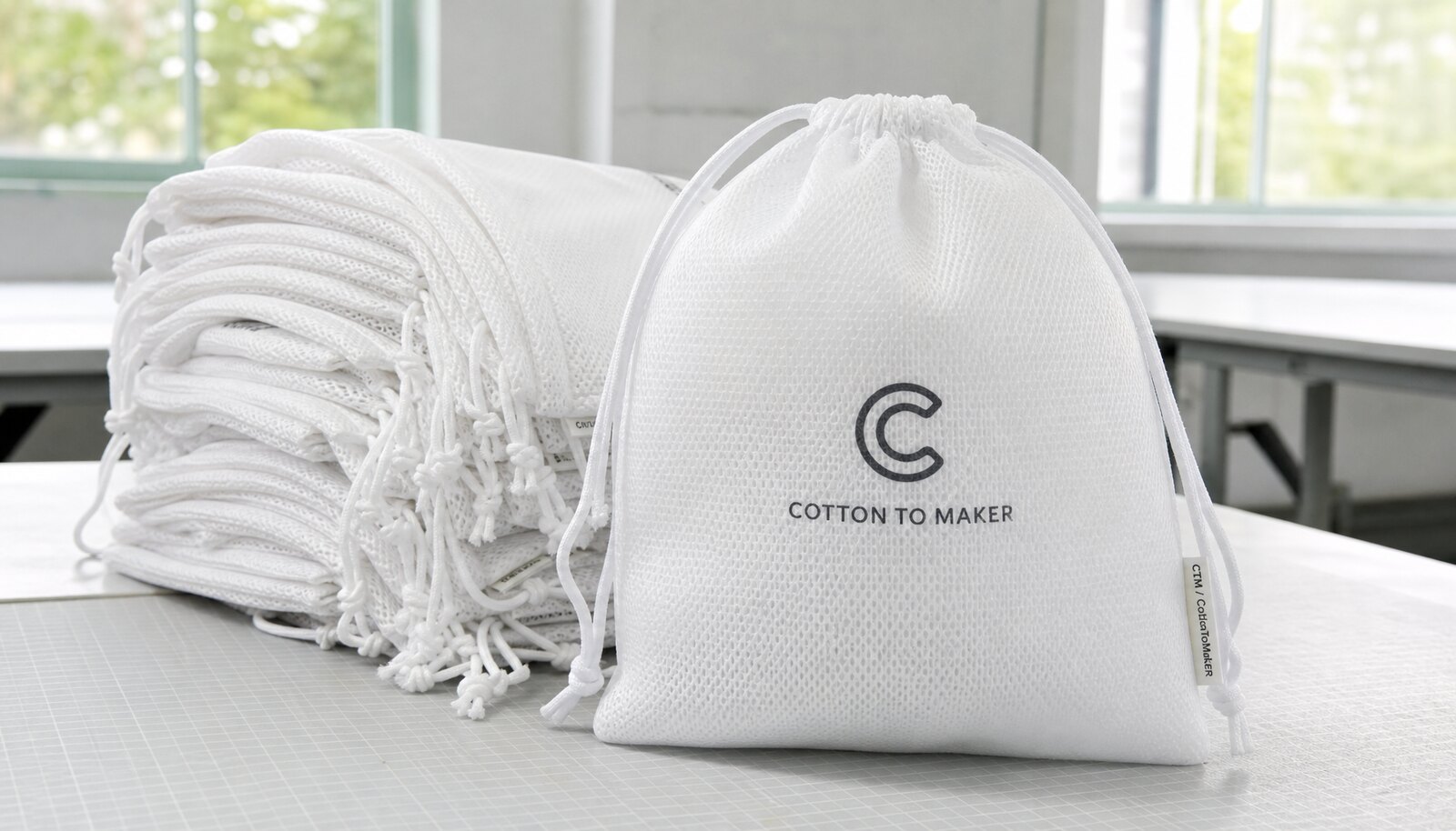 White personalized mesh drawstring bags with a small CTM side label and simple printed logo in a factory sample room