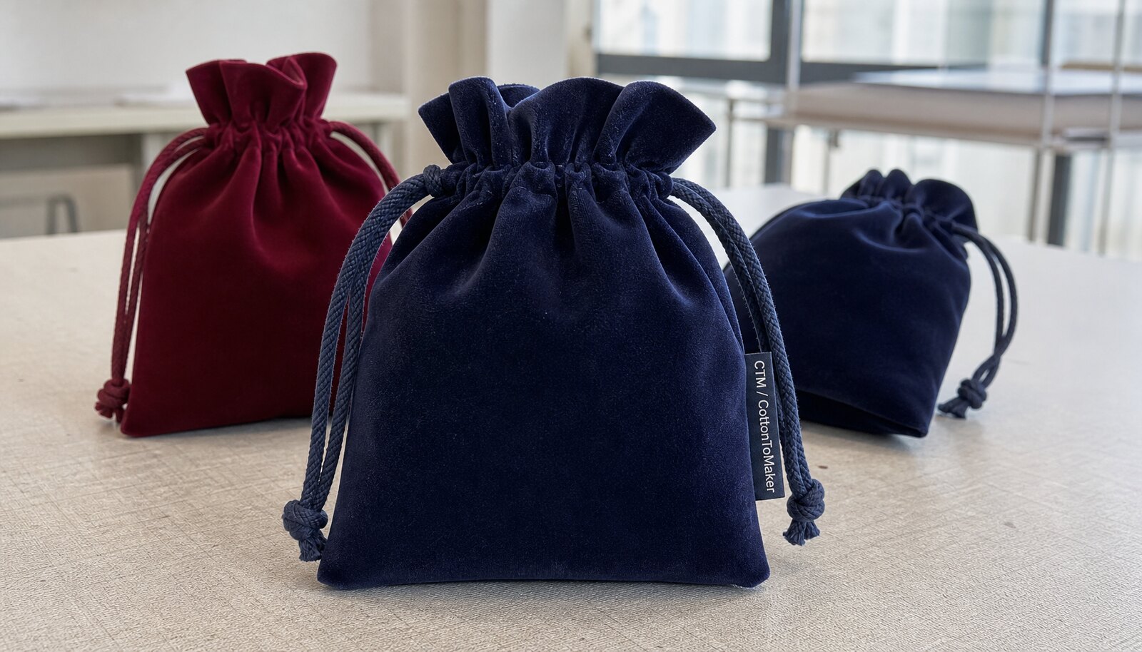 Velvet drawstring pouches with a CottonToMaker woven side label in a clean sample room.