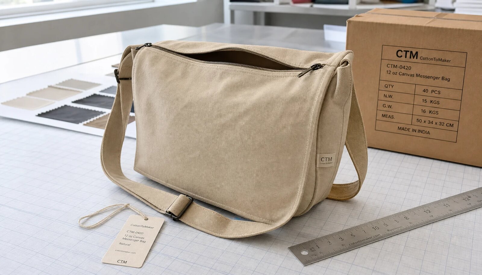 Photorealistic canvas messenger bag sample with a stitched CTM side label, sample carton, ruler, and color swatches in a factory sample room.