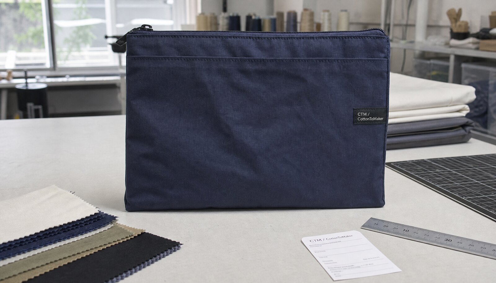 Navy zippered portfolio bag with a sewn CTM side label in a factory sample room